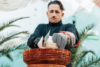 Koch in Schutzhandschuhen öffnet eine Kokosnuss mit einer Machete an der Foodstation