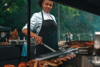 Eine Köchin in schwarzer Schürze bereitet Würstchen auf dem Grill zu